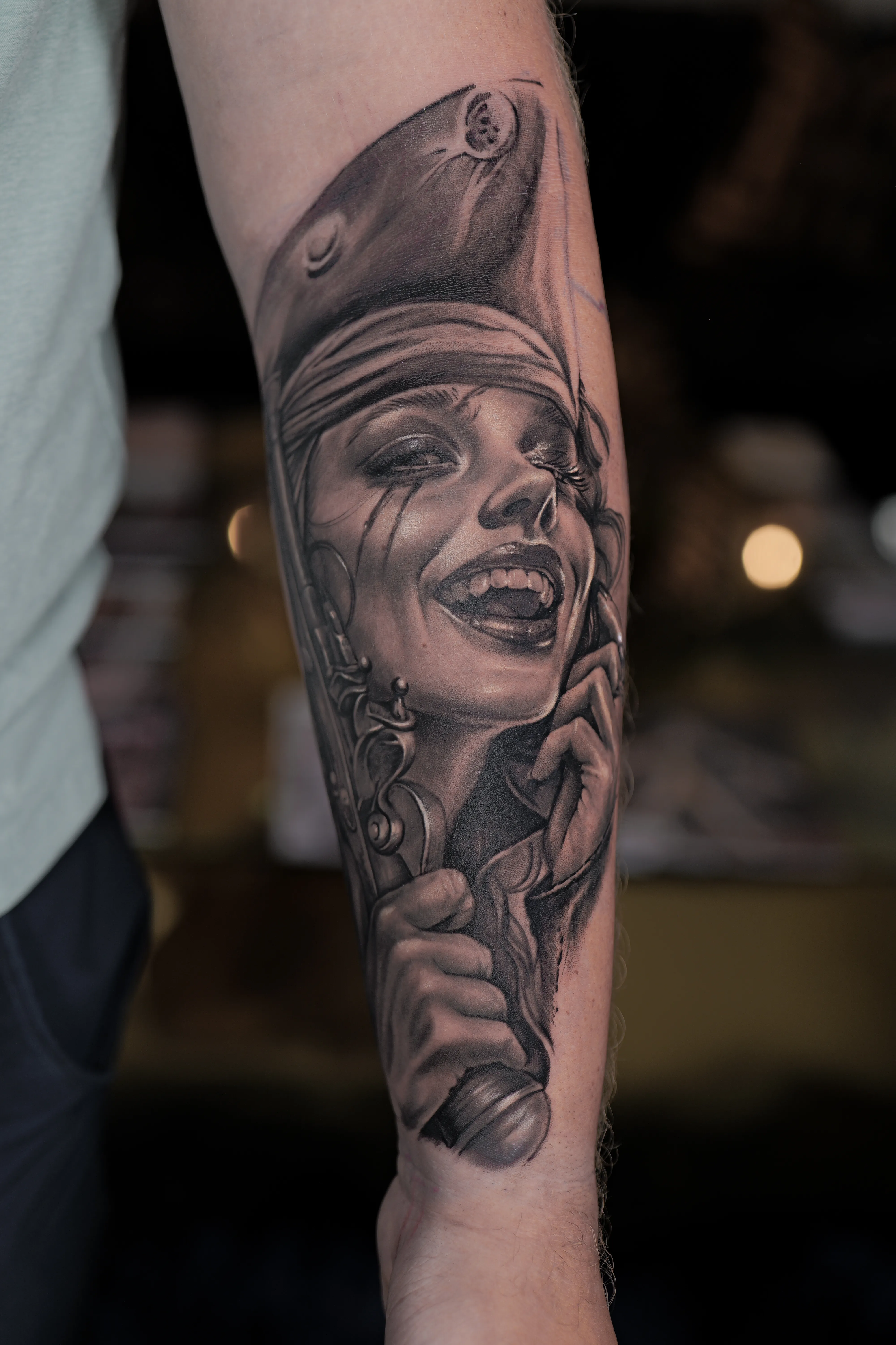 Black-and-grey realism forearm — laughing pirate woman with a flintlock pistol and rose — Hector Rodriguez Goderich