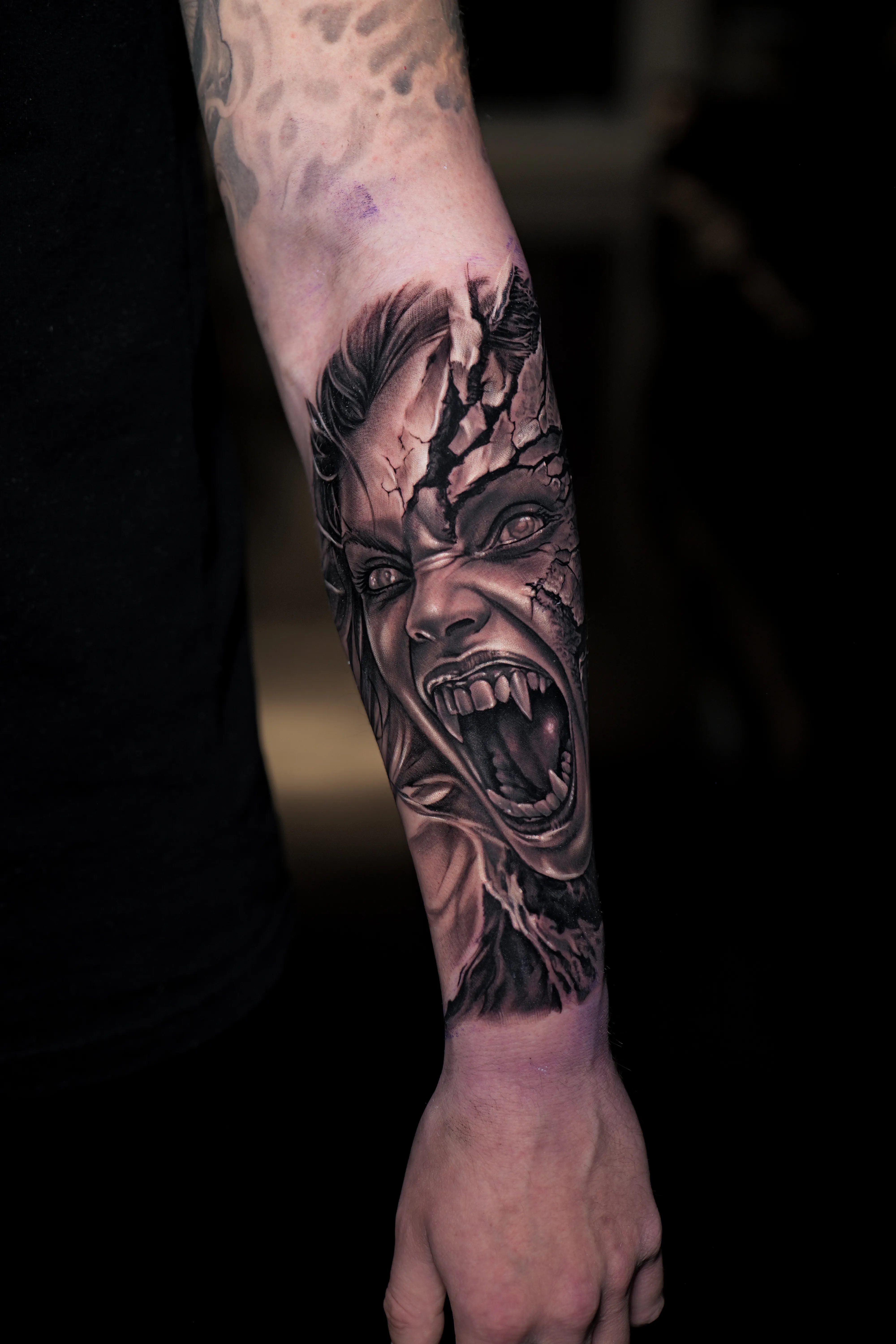 Black-and-grey horror realism — screaming demon with cracked stone skin bursting from the arm — TKOTATTOO