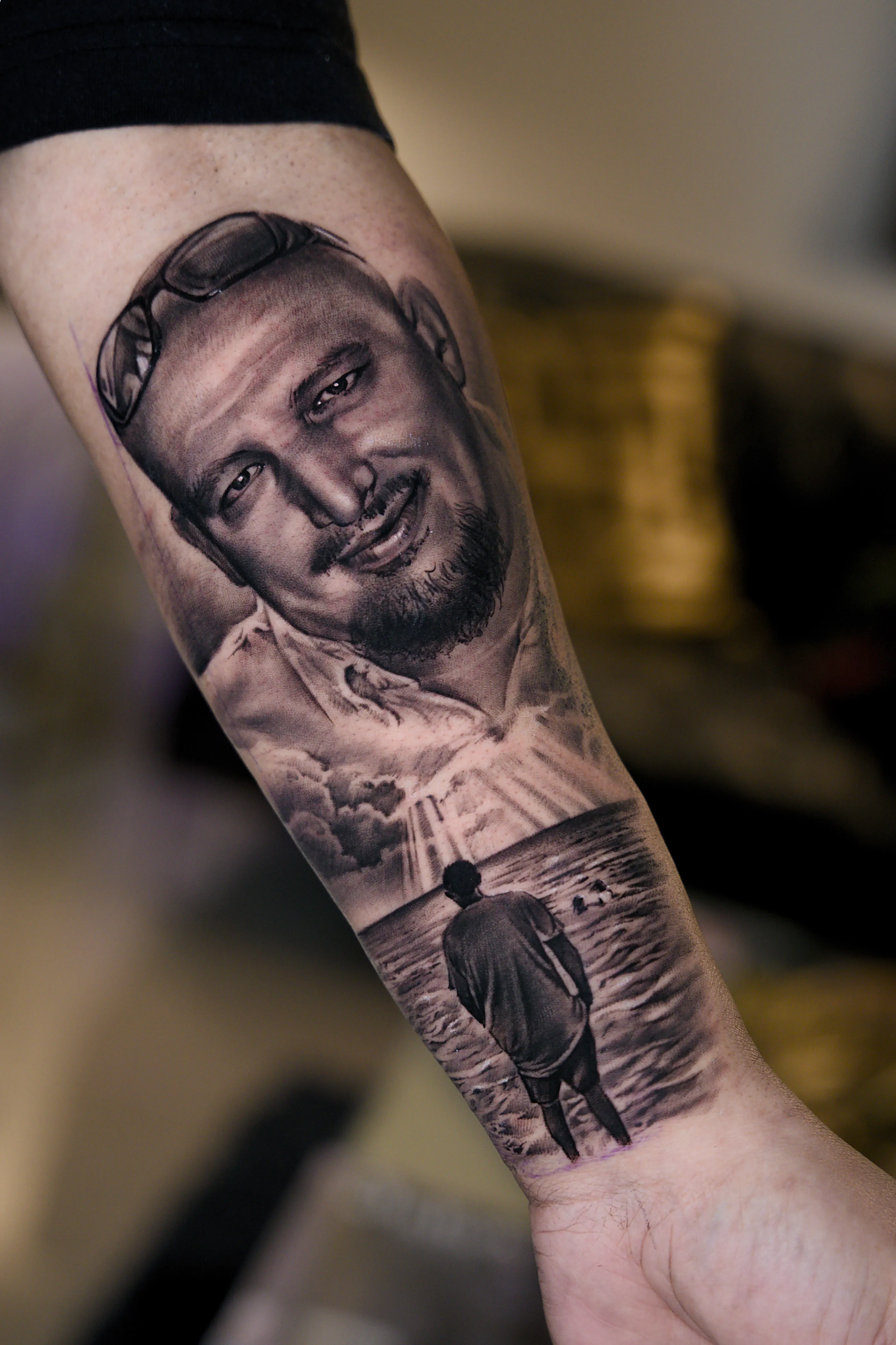 Black-and-grey memorial portrait of a smiling man above a figure walking into the sea under light rays — TKOTATTOO