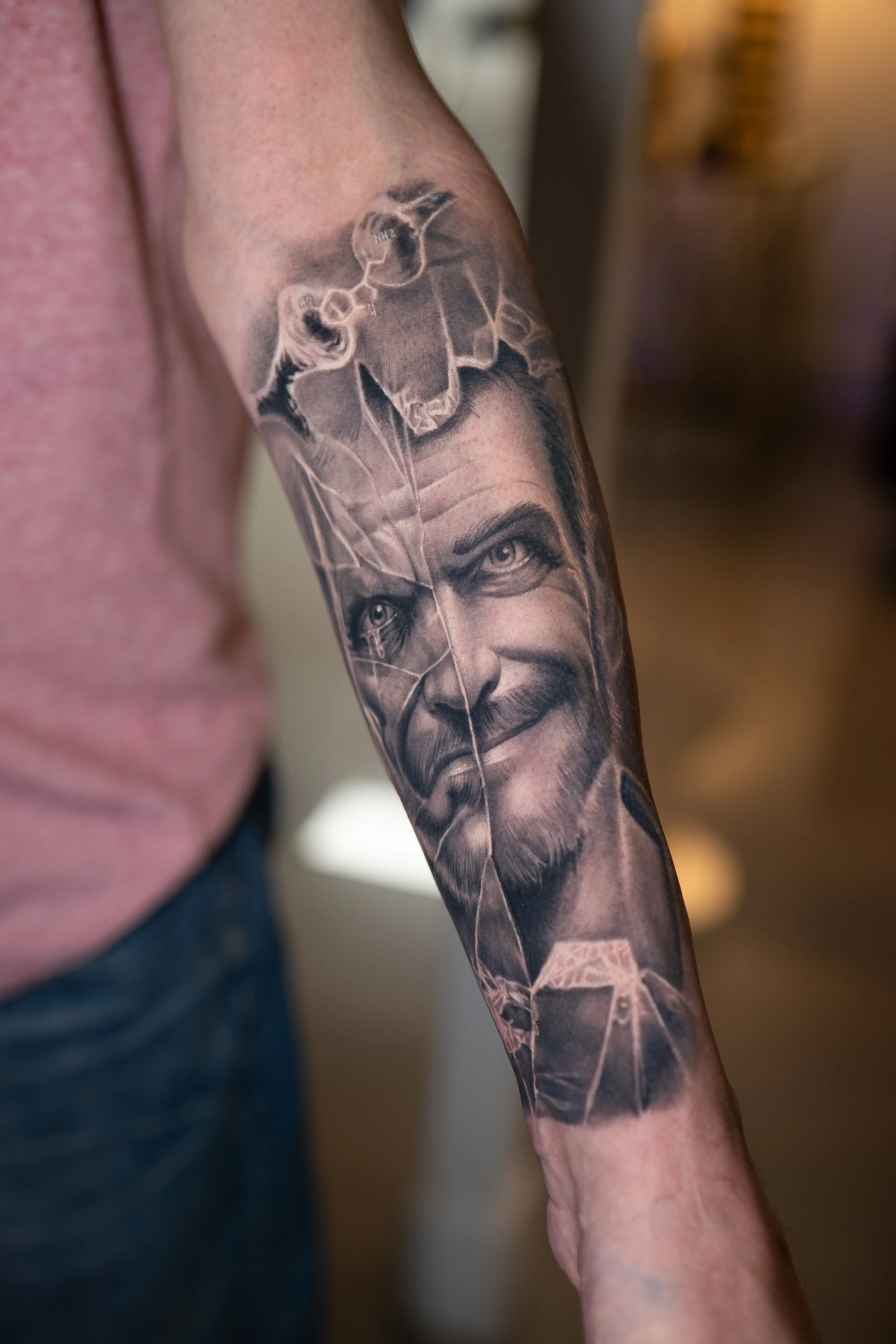 Black-and-grey realism — a smiling man’s portrait fractured like broken glass with a molecule motif — TKOTATTOO